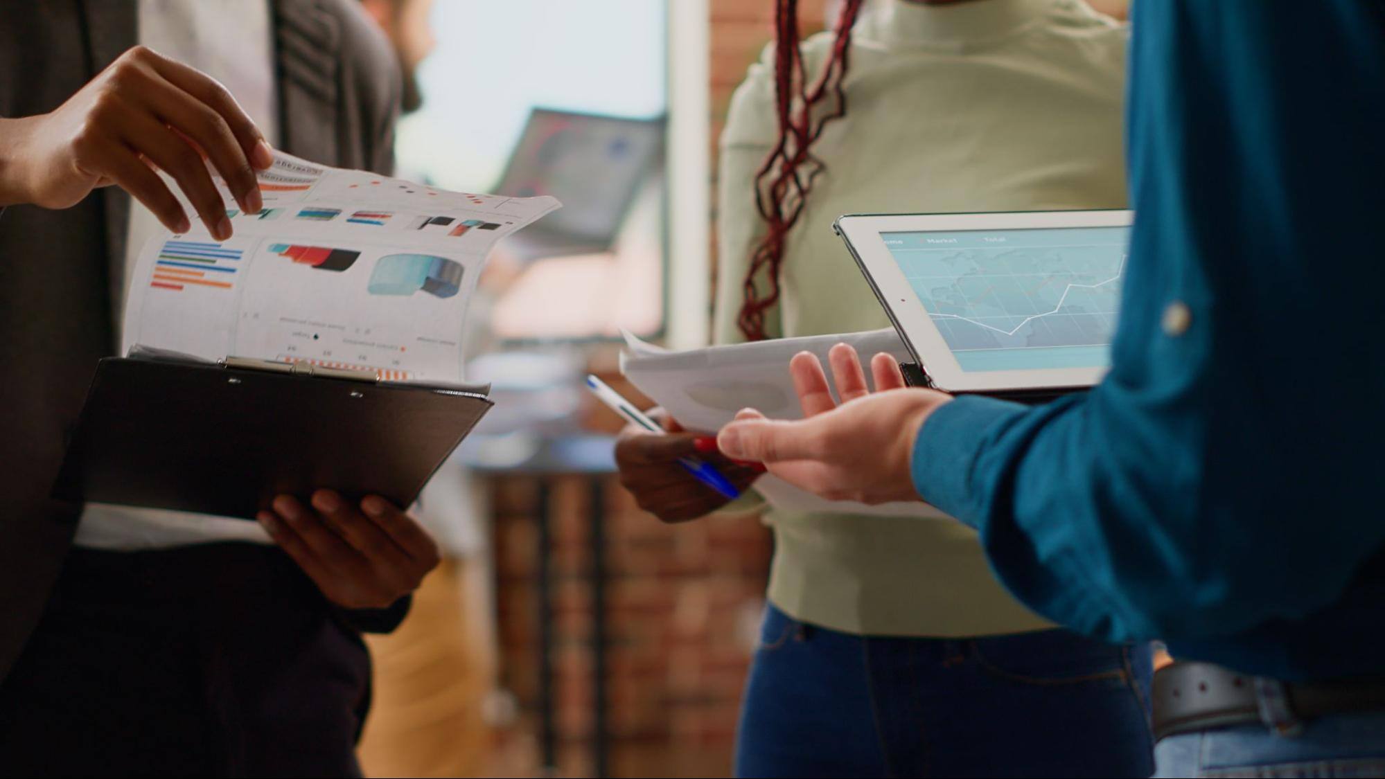  Three people using iPads and looking at charts printed on pieces of paper.&nbsp;