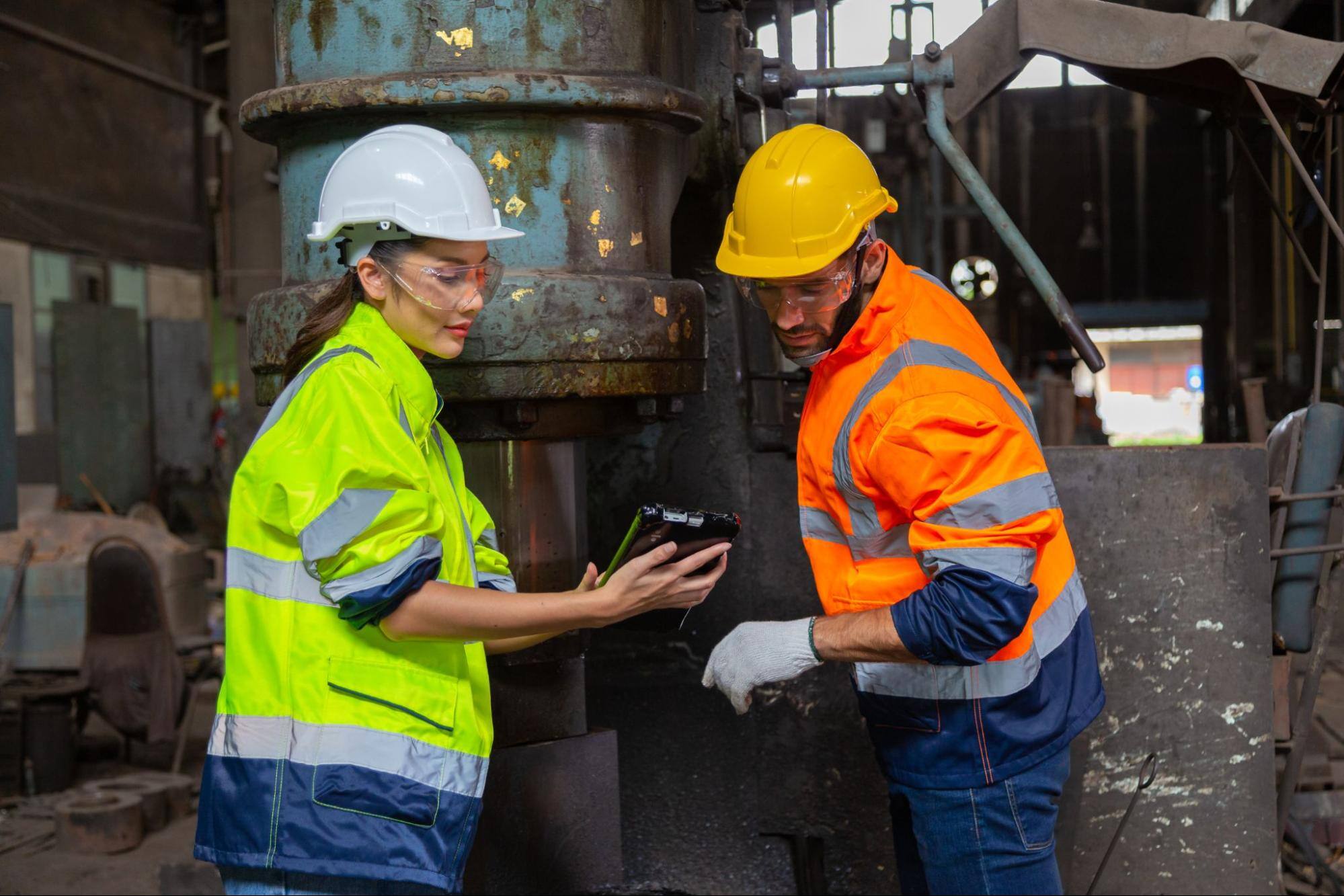 Two construction workers wearing hard hats and goggles looking at a tablet.&nbsp;