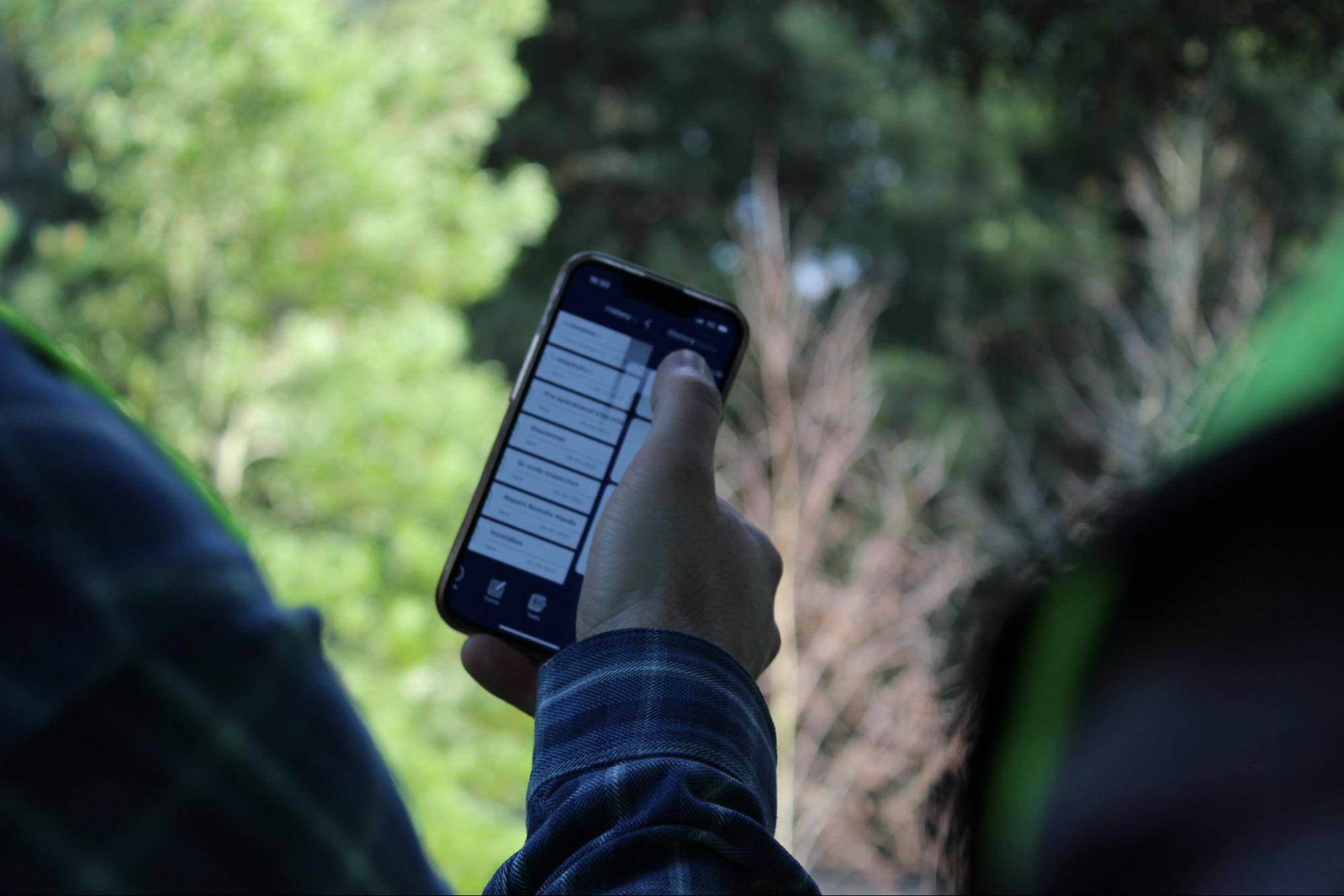 Person using a cell phone with trees in the background. 