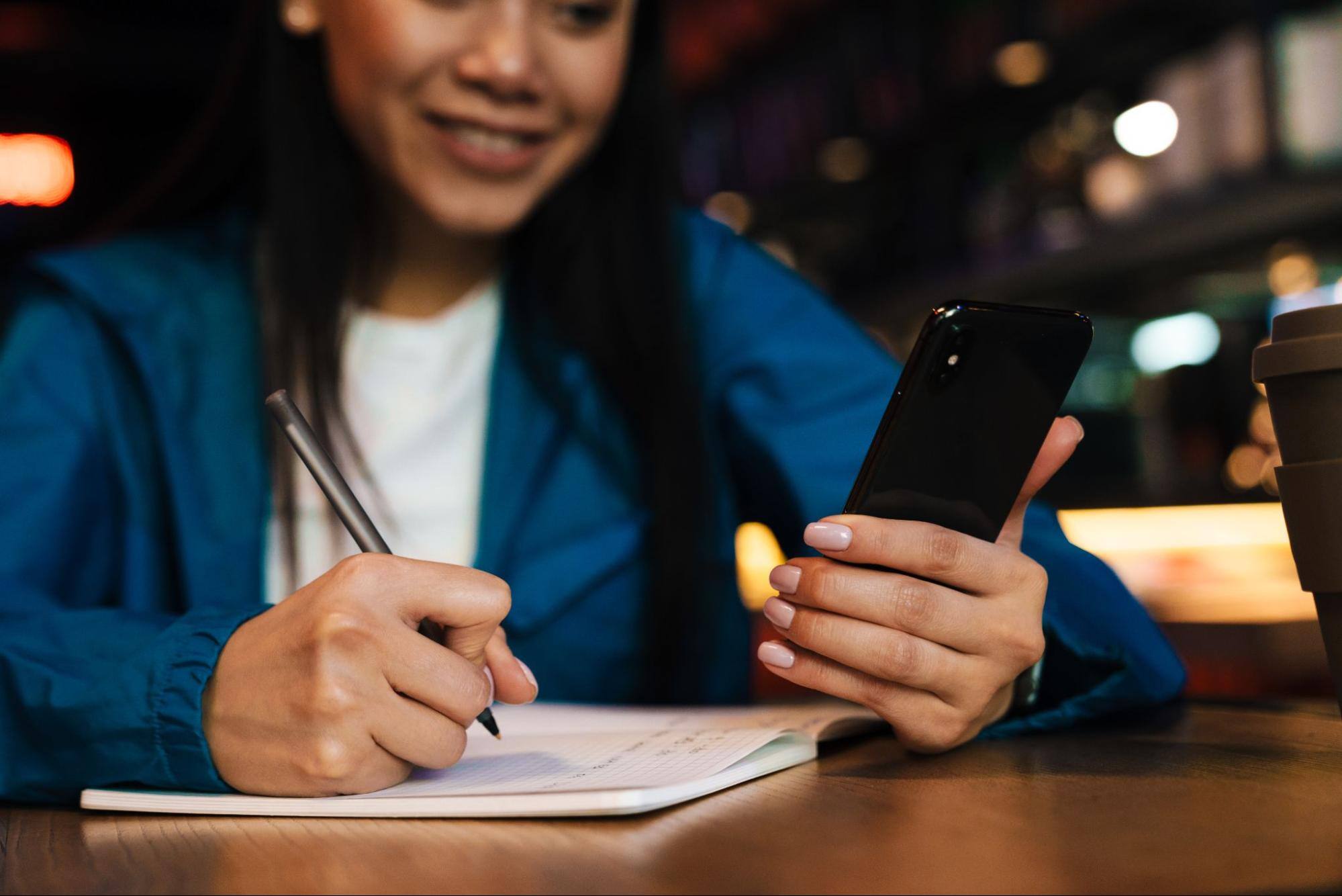 Woman using a cell phone and taking notes. 