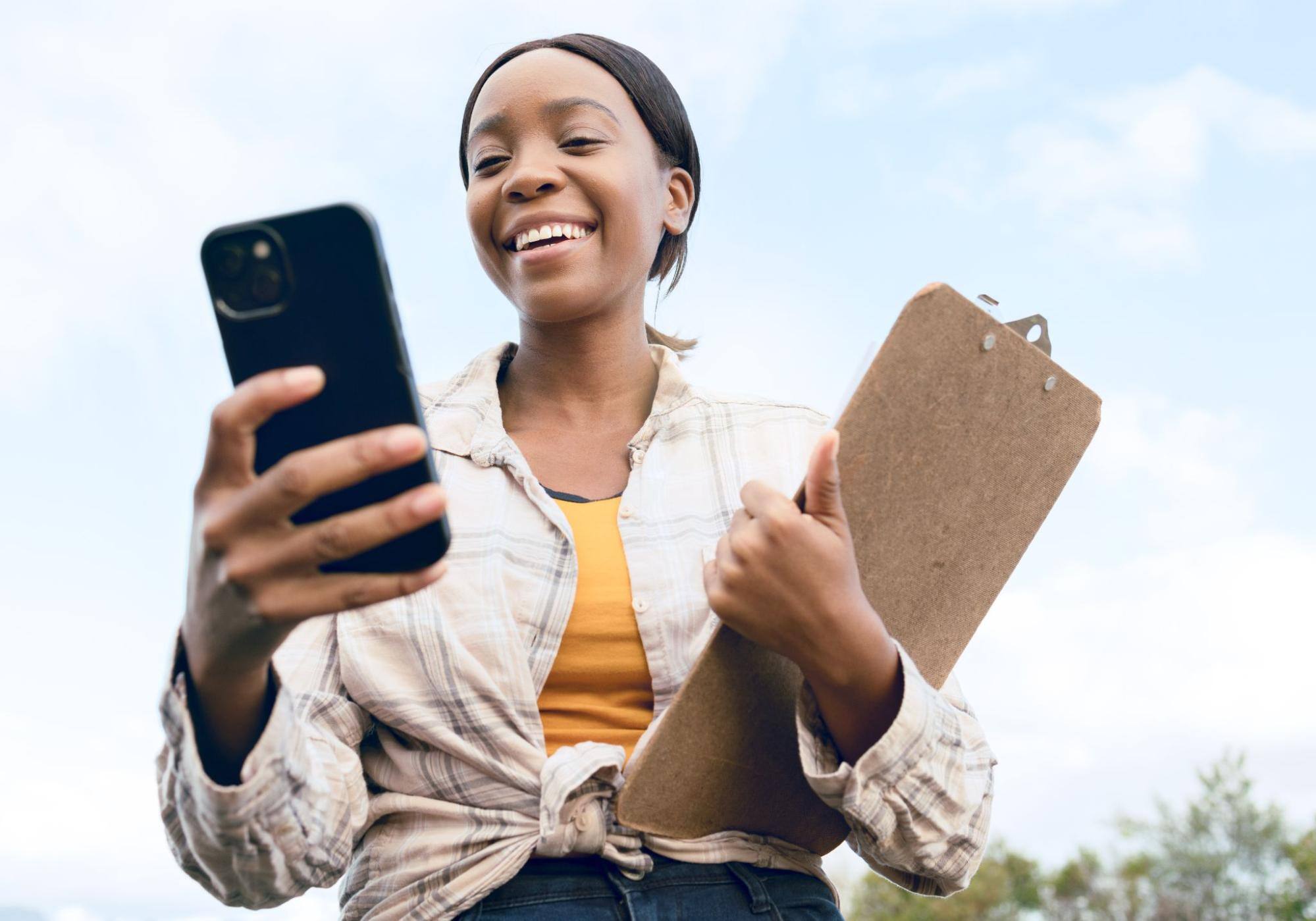 Smiling woman holding a clipboard and using a phone.