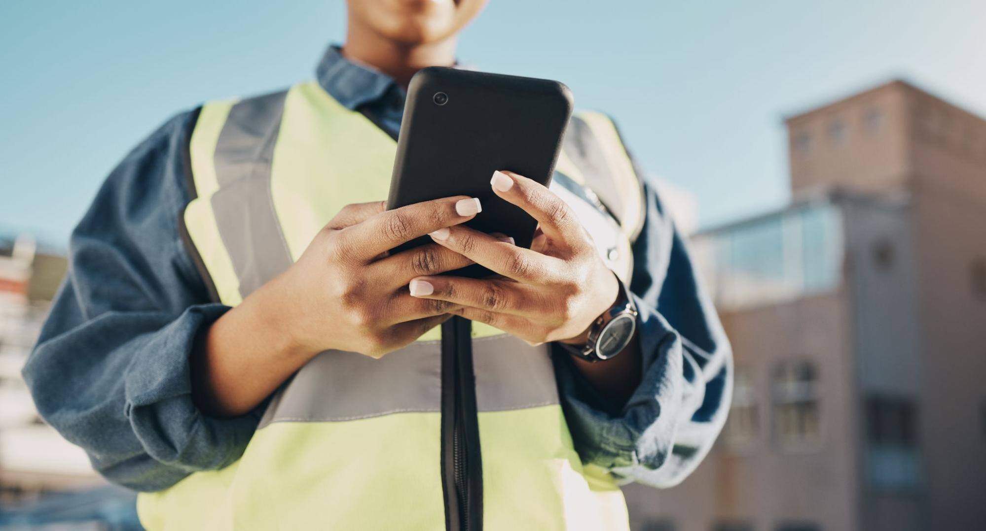Woman wearing a construction vest and holding a phone. 