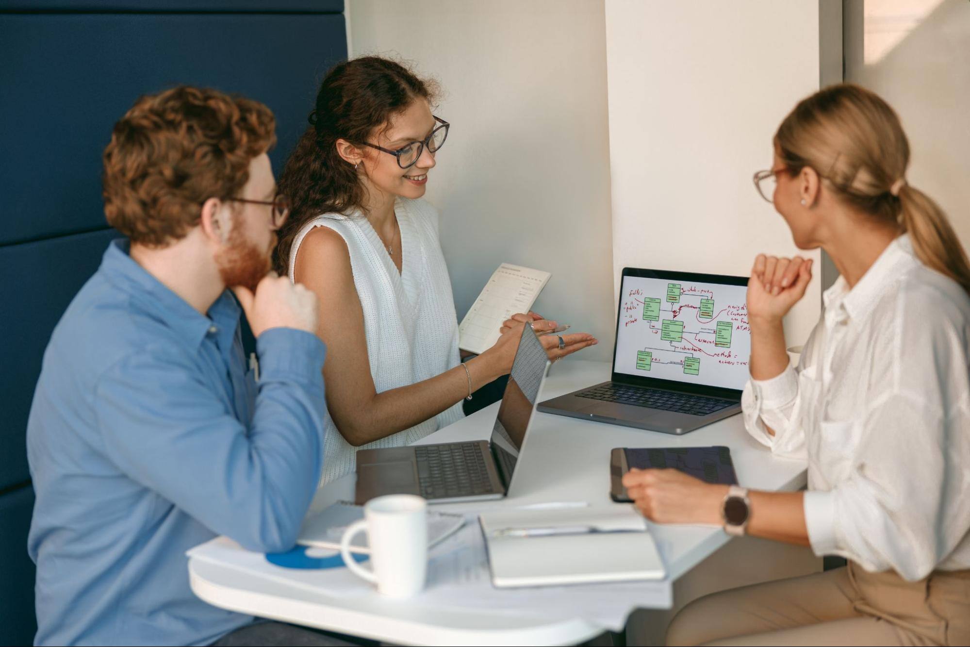 Two women and one man in a meeting business office working together and looking at information on a laptop.