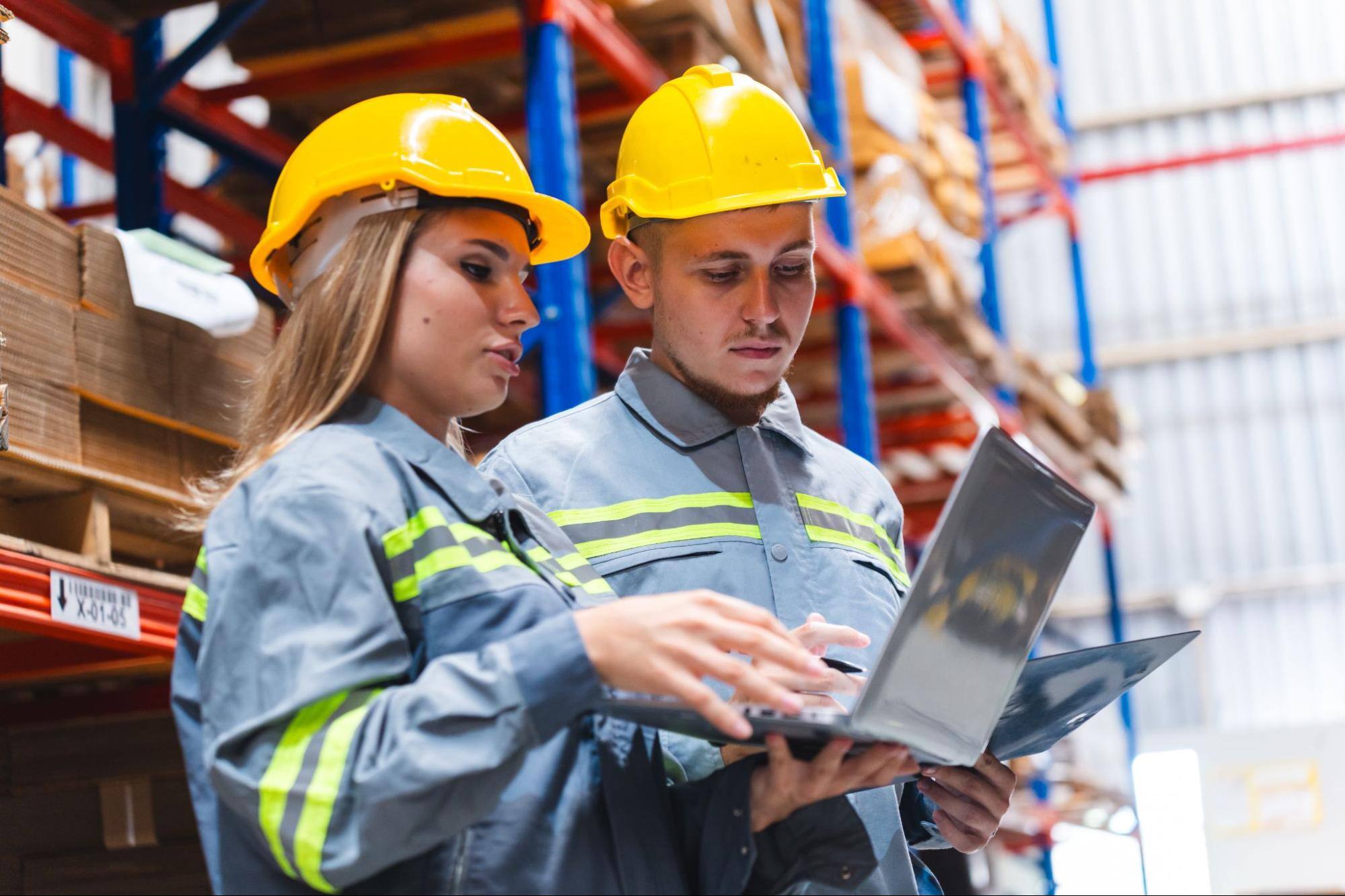 A lady manager and worker in safety gear use supply chain software to check real-time inventory in a warehouse.