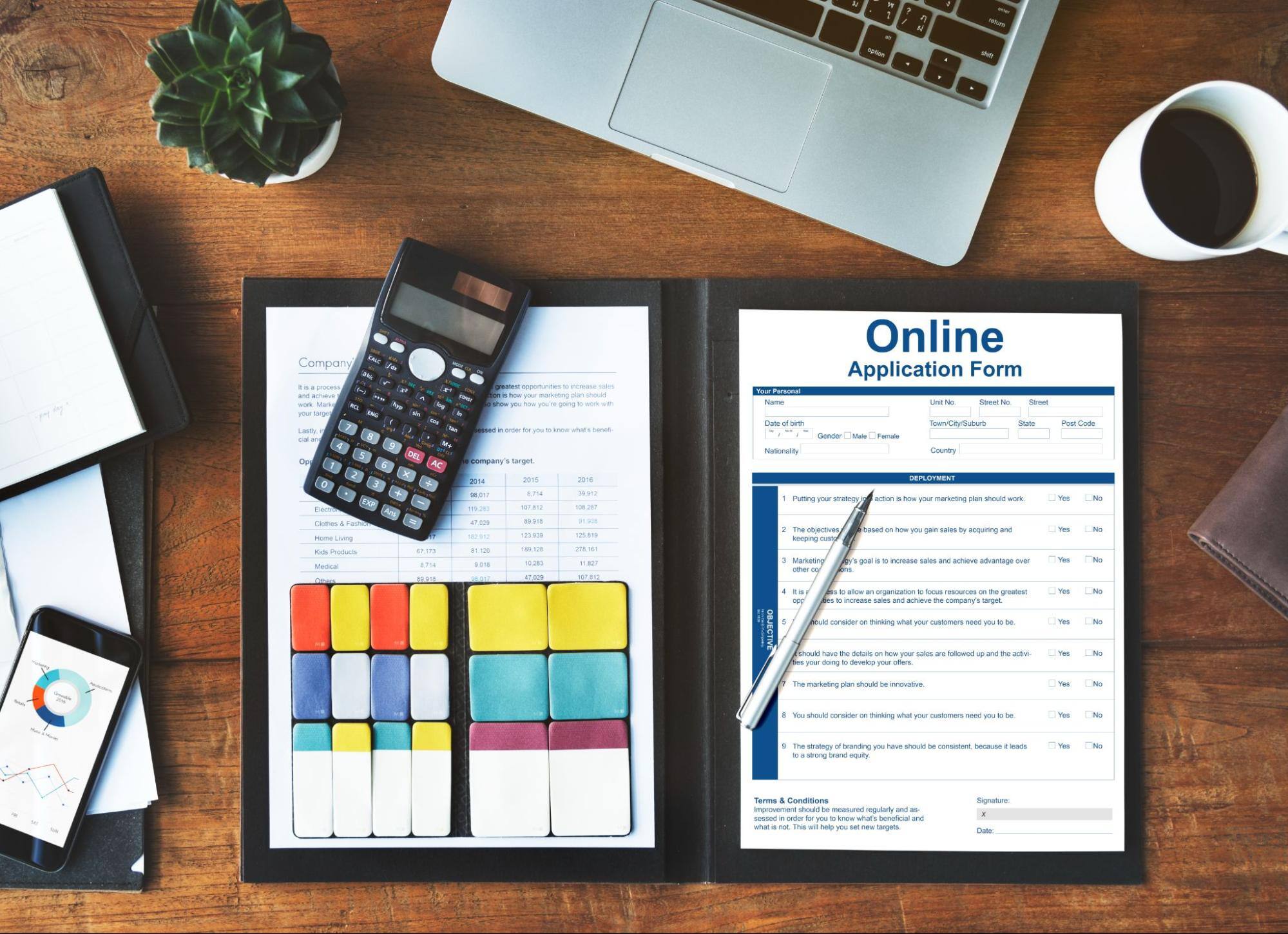 Creating digital forms using traditional paper forms, color-coded sheets, a laptop, a calculator, and a cup of coffee for a productive workspace.