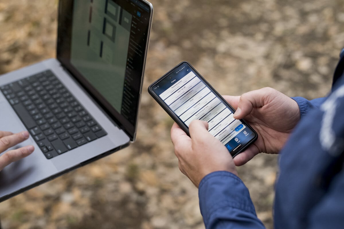Mobile form on a computer and cell phone with a view of two hands. 