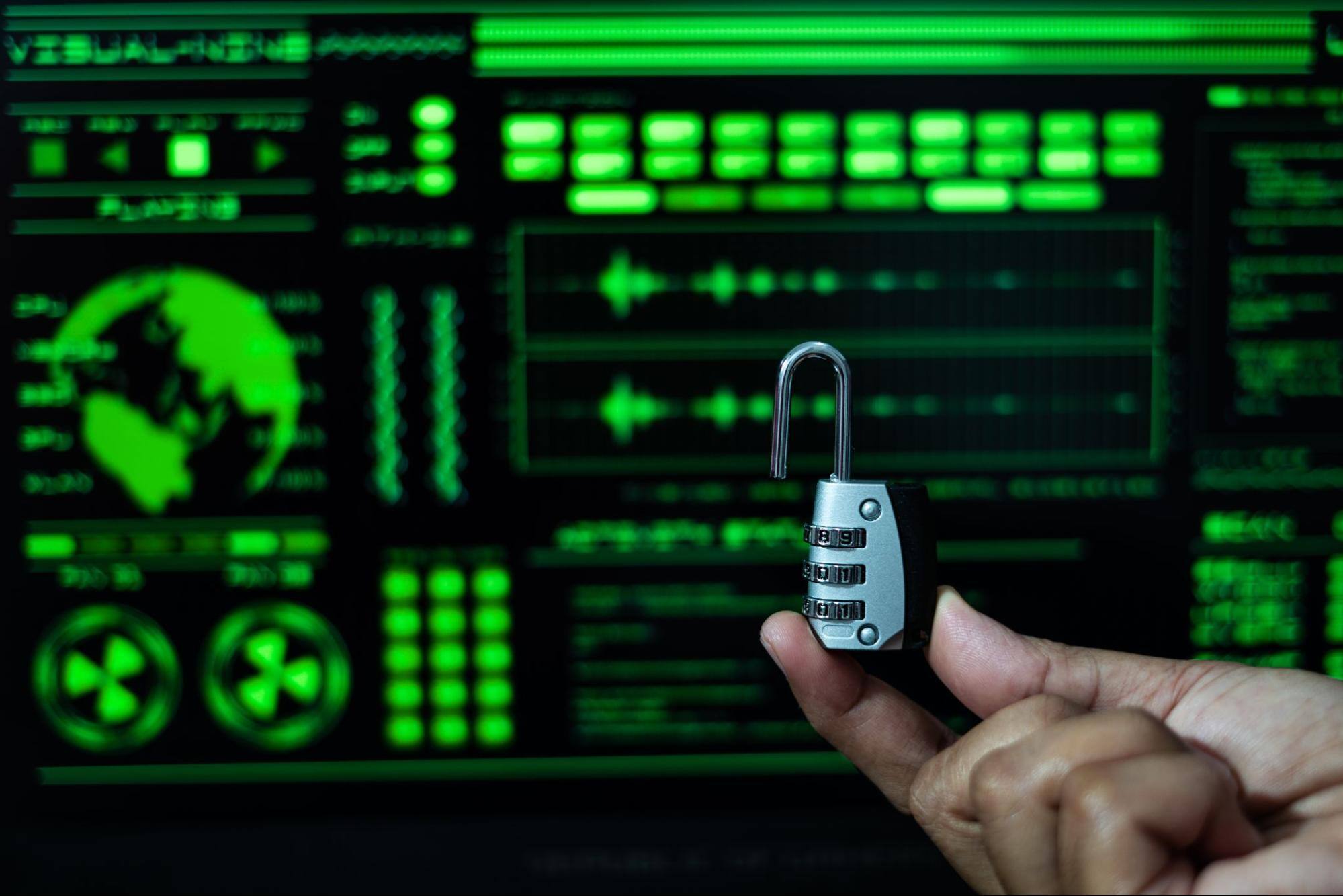Cropped view of someone's hand holding up a lock with a green and black digital background.