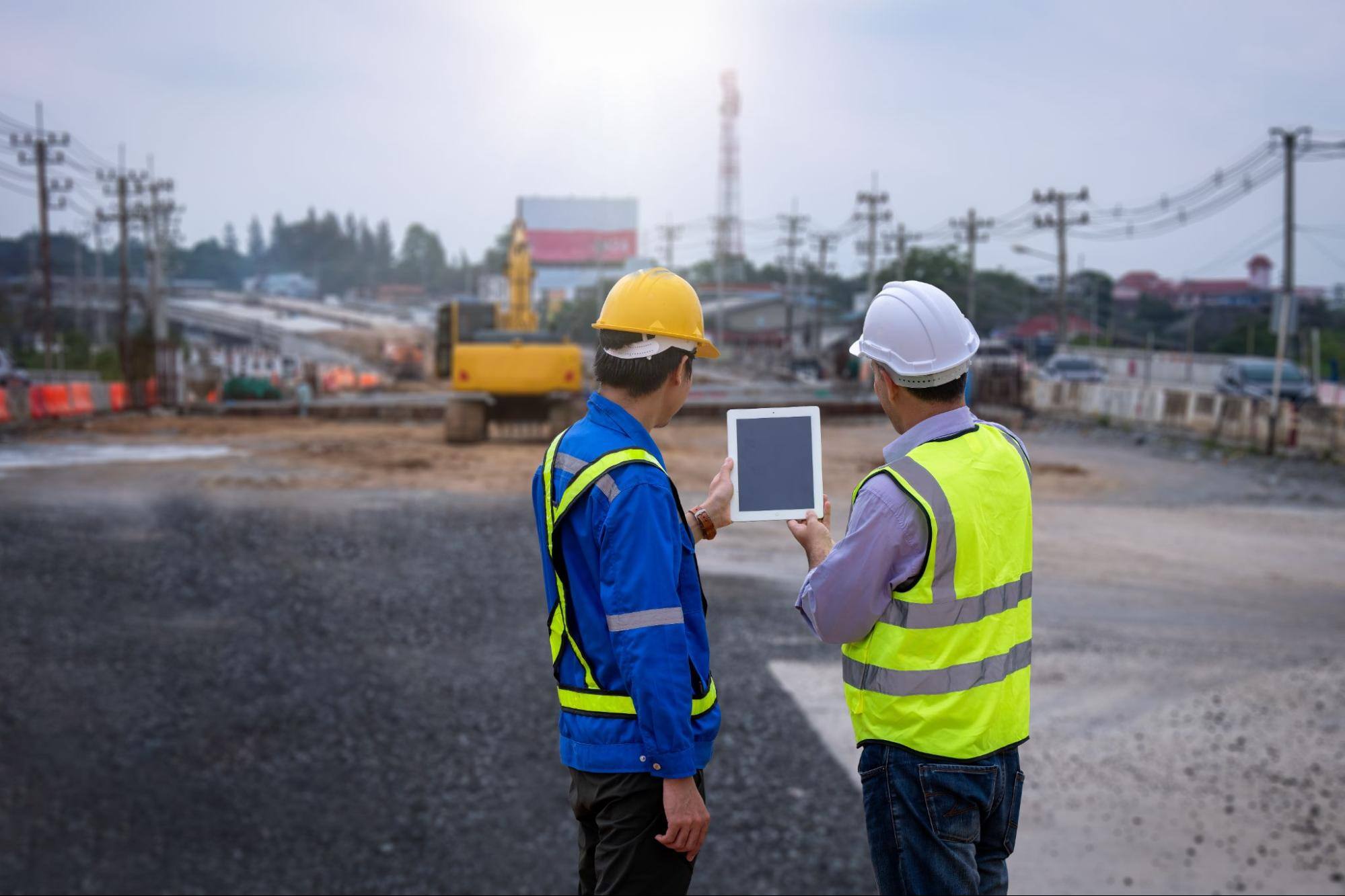Construction workers using a tablet with a crane in the background. 