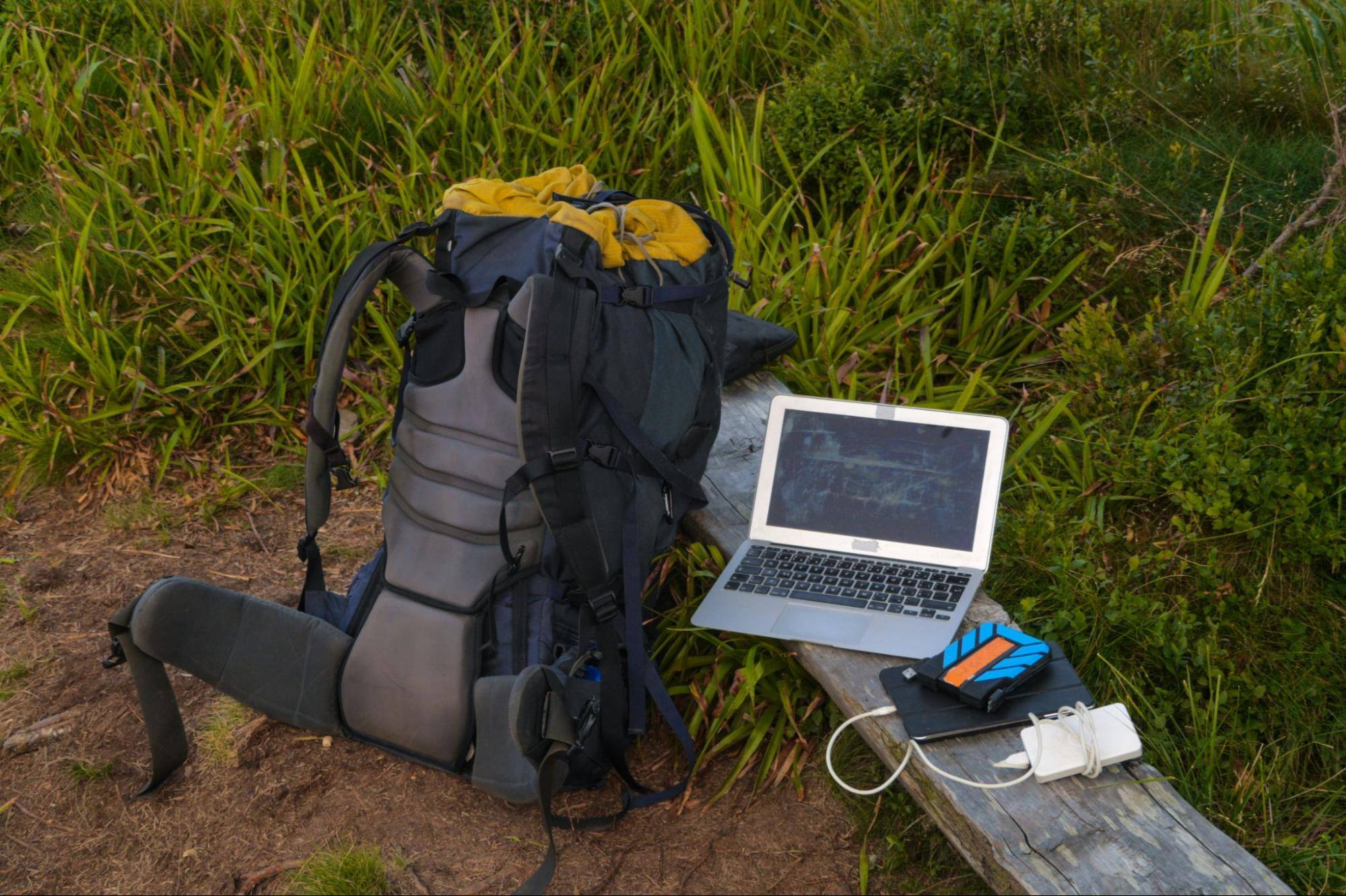 A display of workforce management technologies set in a forest, featuring a solar panel, tablet, laptop, and backpack to demonstrate mobile, portable solutions.