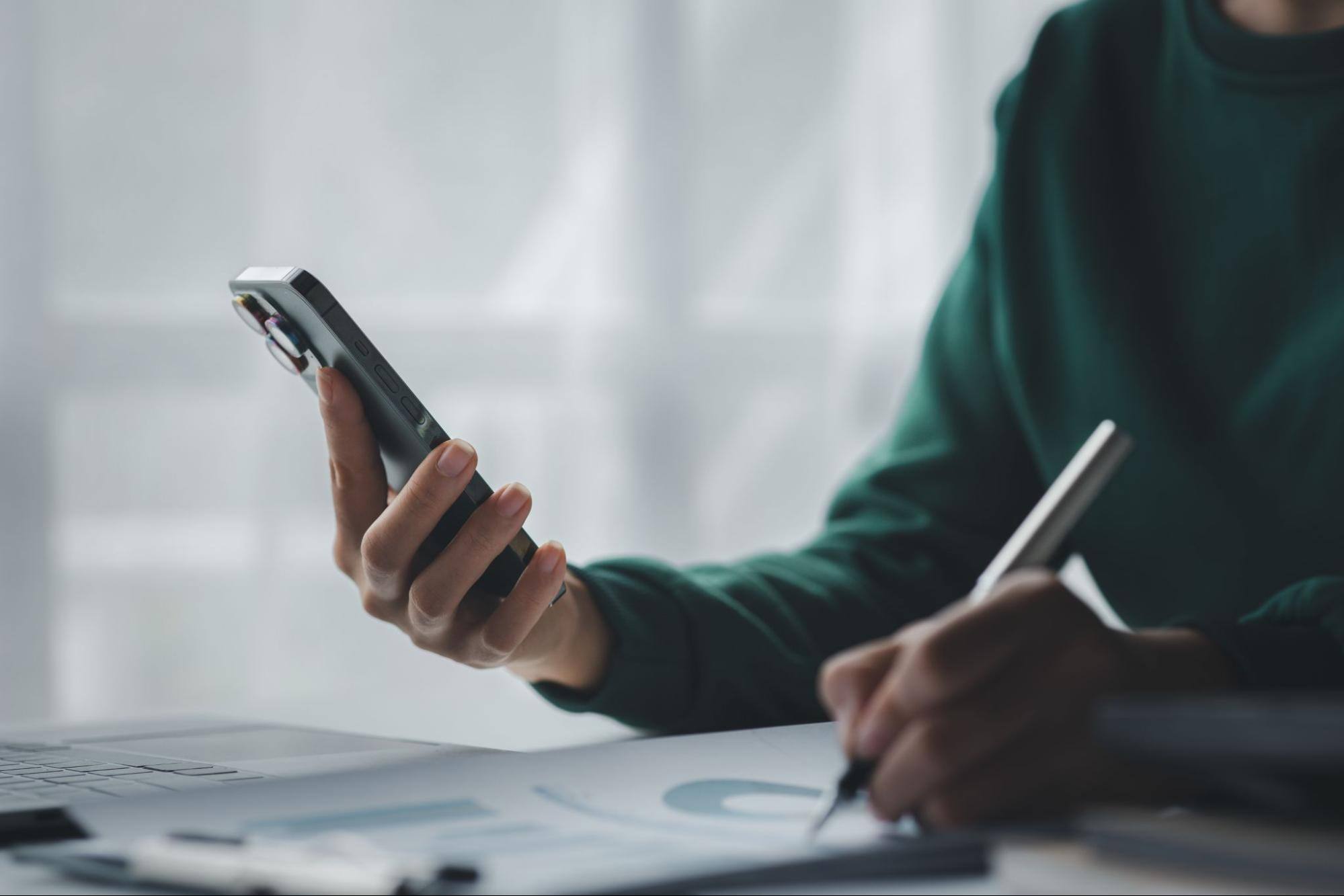Woman using a phone and writing on a piece of paper. 